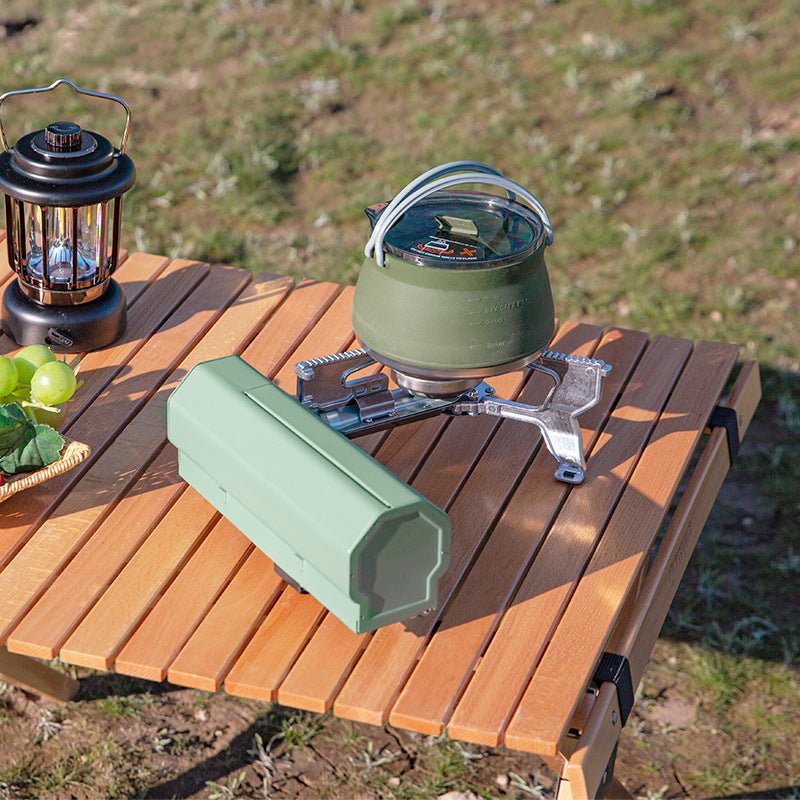 Portable Camping Gas Stove on wooden table outdoors, featuring folding design and green storage case.